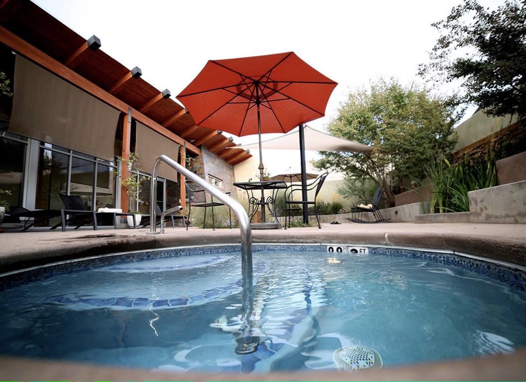 The spa's outdoor hot tub under a red umbrella, beside the adobe building