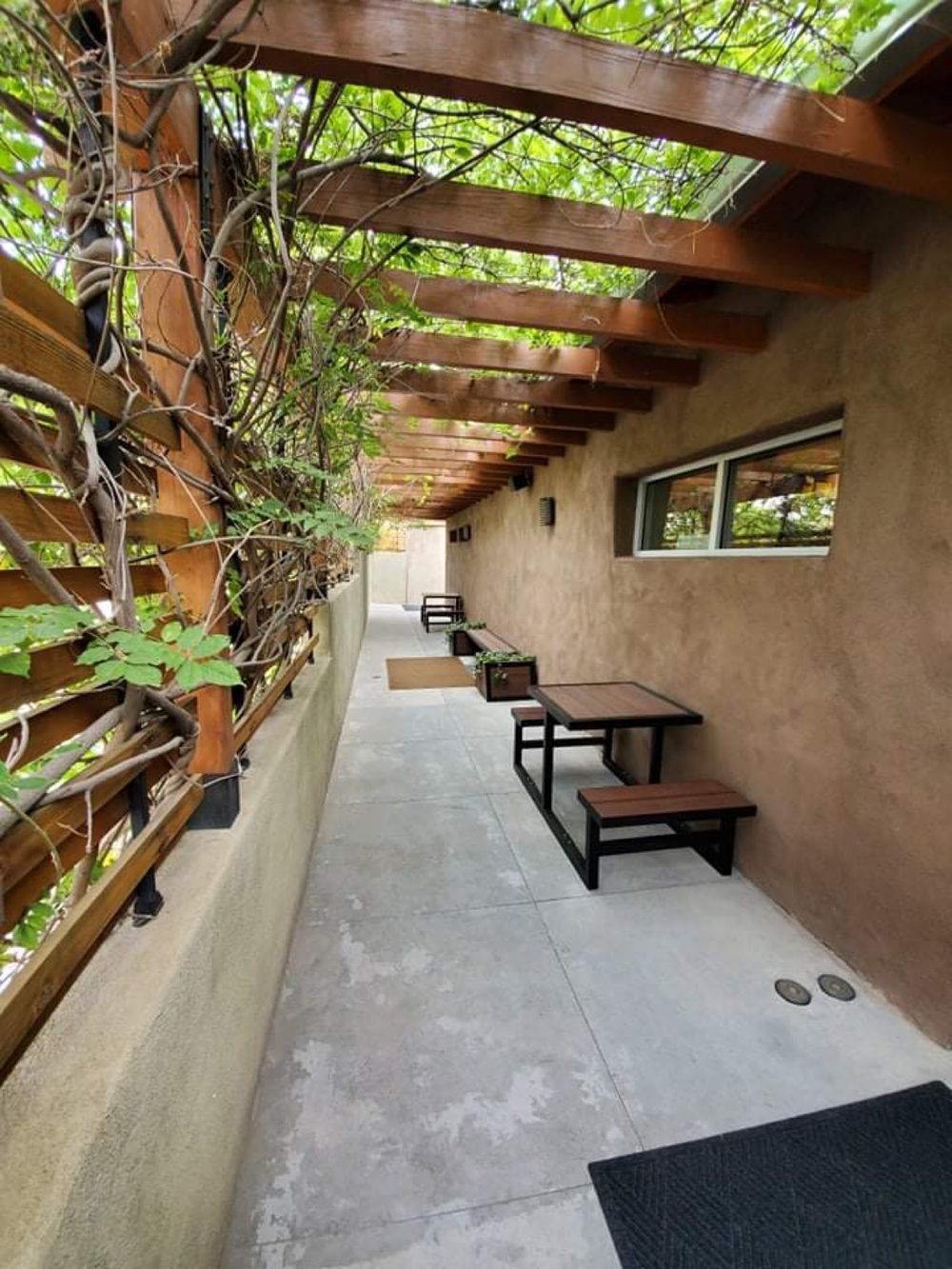 A shaded pergola walkway along the spa's adobe wall, with benches and climbing vines