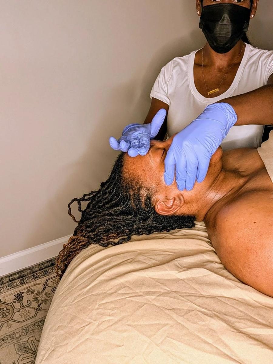 A therapist in blue gloves and a face mask giving intra-oral TMJ massage to a woman lying on a massage table