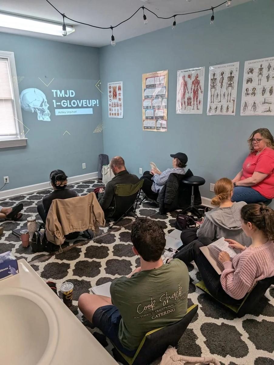 Students seated on the floor of a classroom before a projected TMJD 1-Glove Up! slide