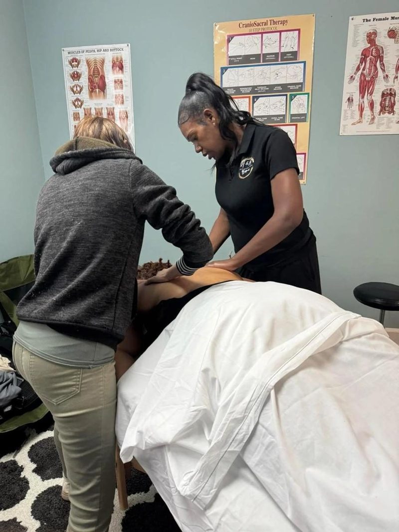 Ashley guiding a student's hands at the massage table