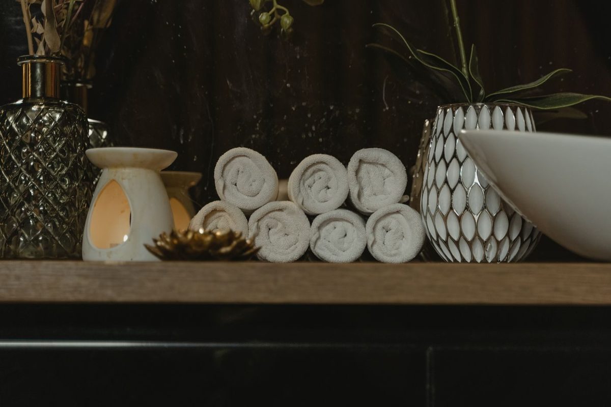 Warm rolled towels on a wooden shelf beside a glowing oil burner